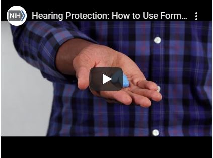 A screenshot of video depicting an adult hand holding formable earplugs.