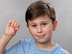 A boy holds a formable foam earplug between three fingers.