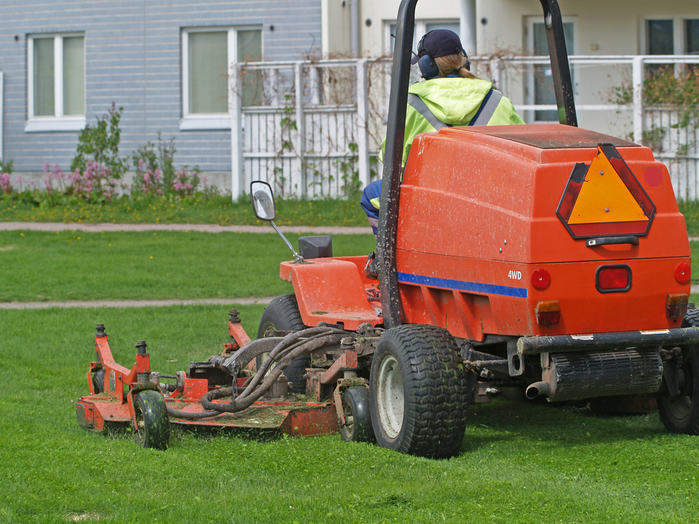 A large mowing tractor being driven across a lawn by an adult male.