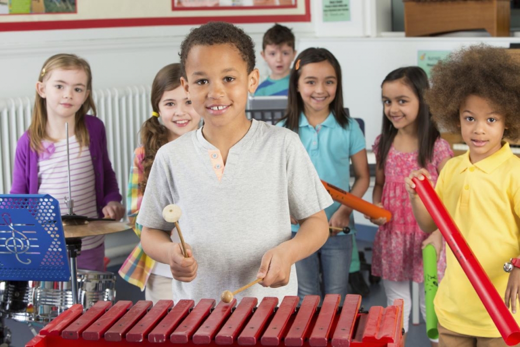 Un aula con varios niños con instrumentos musicales, con un niño tocando el xilófono.