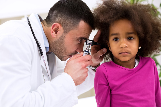 A pediatrician examines a young girl's ear with an otoscope.