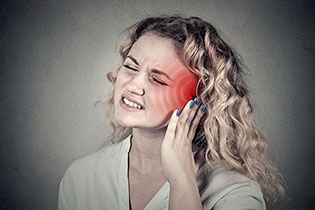 A young woman wincing in pain while pressing against her ear.