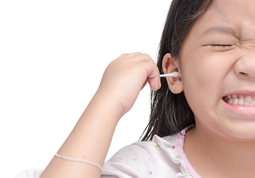 A young girl wincing as she cleans her ear with a cotton swab. 