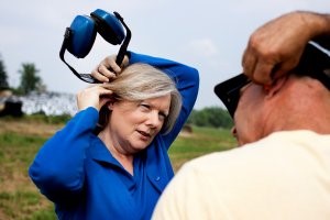 Marjorie McCullagh, the study author, holds protective ear muffs in one hand as she demonstrates to a farm worker how to properly insert ear plugs.