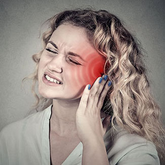 A young woman holds her ear while grimacing in pain.