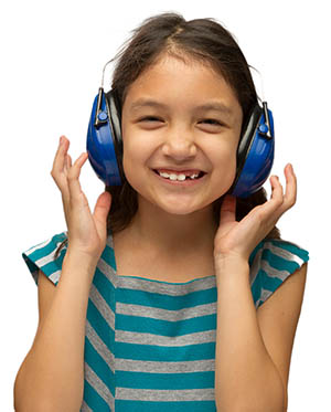 A girl smiles and wears protective earmuffs.