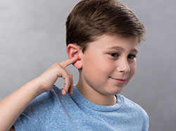 A boy uses his index finger to touch the tip of a formable foam earplug in his ear and hold it in place. 
