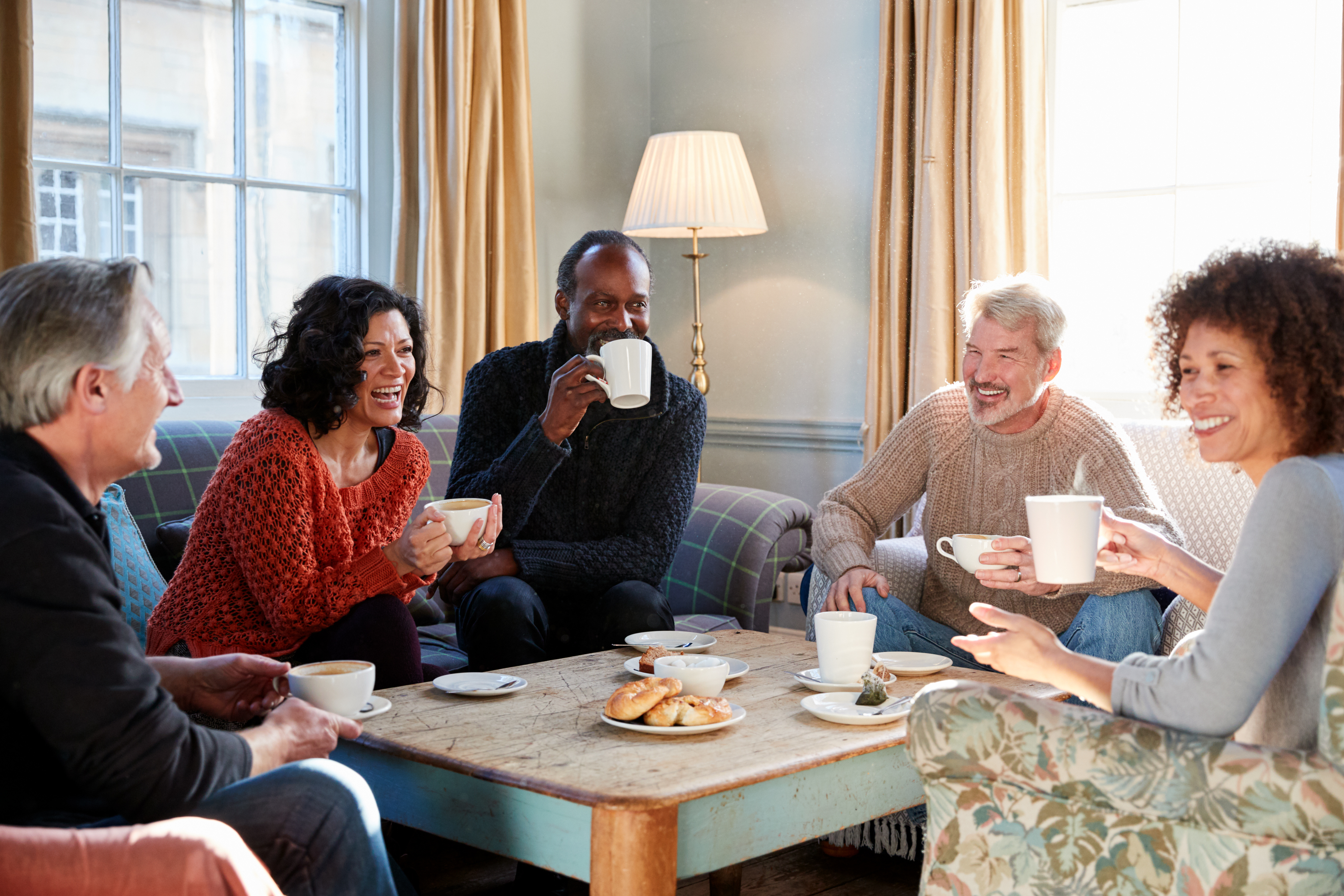 Group Of Middle Aged Friends Meeting Around Table In Coffee Shop.