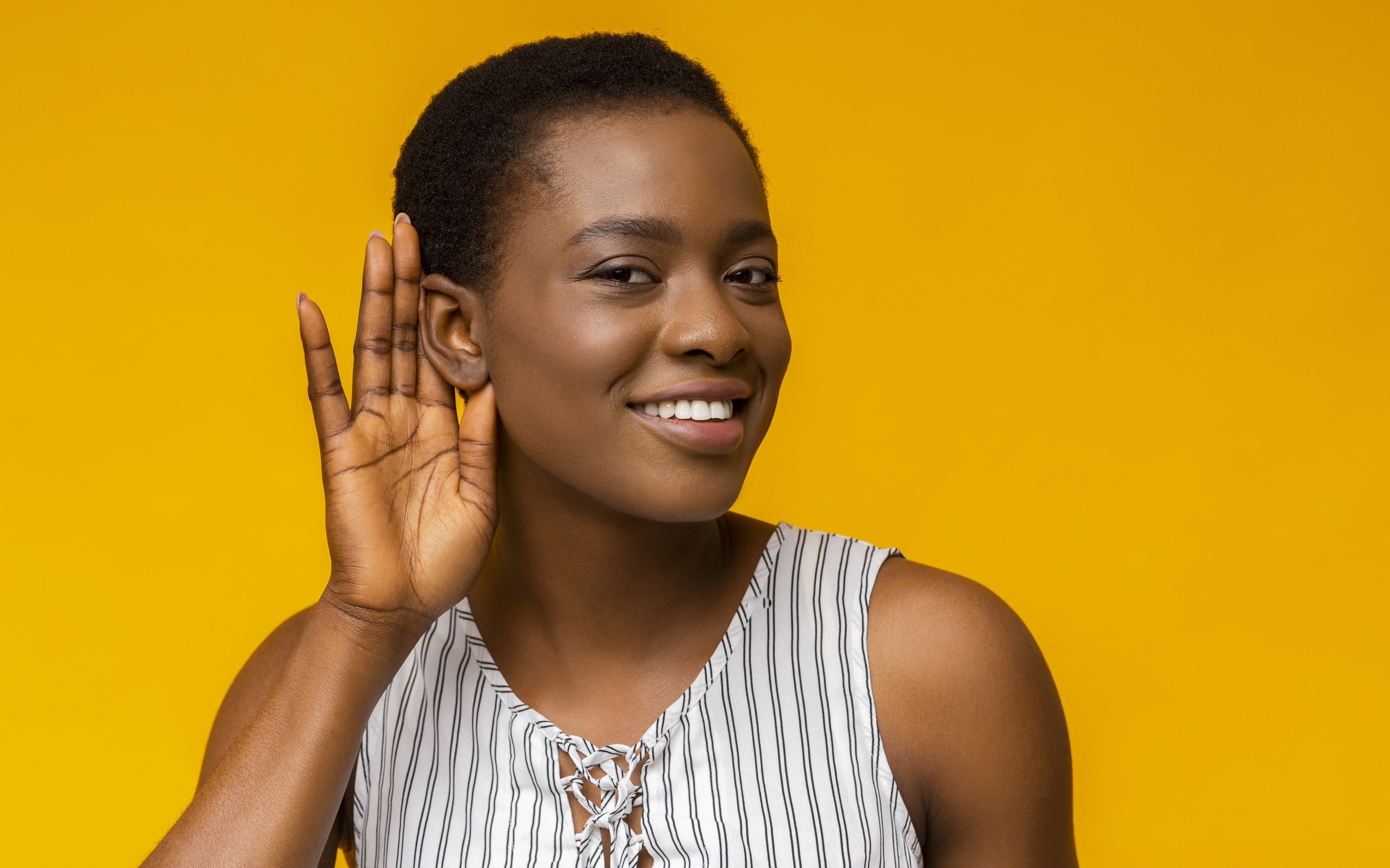 Woman holding her hand up to her ear as if to better hear something.