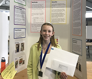 13-year-old Nora Keegan stands in front of a poster presentation detailing her research.
