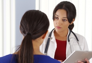 A female medical professional holding a computer tablet speaks to an adult female.