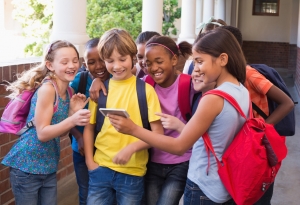 A group of children standing in the hallway of a school looking at a mobile device.
