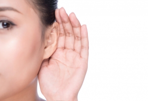 Una mujer joven con una mano sobre su oído intentando escuchar. 