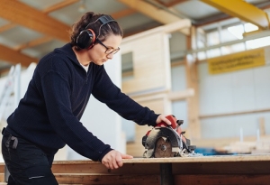 A woman uses a circular saw while wearing protective earmuffs.