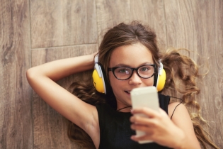 Tween listening to device with headphones on and lying down on her back on the hardwood floor.