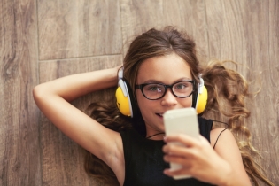 Una preadolescente escuchando música con un dispositivo y usando orejeras.