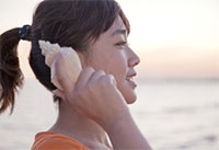 Woman holding a seashell up to her ear with ocean in background