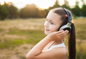 Una niña está al aire libre escuchando música con orejeras.