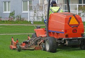 A large mowing tractor being driven across a lawn by an adult male.
